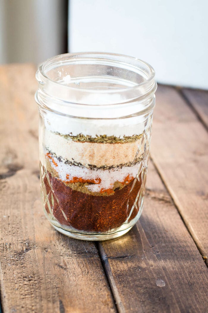 A clear jar displaying stacked layers of spices for DIY taco seasoning.