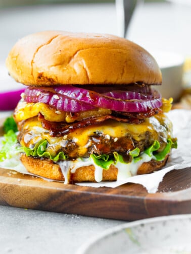 a photo of a cheeseburger topped with melted cheese, slice red onions, grilled pineapple, bacon and a white creamy sauce all in a toasted bun.