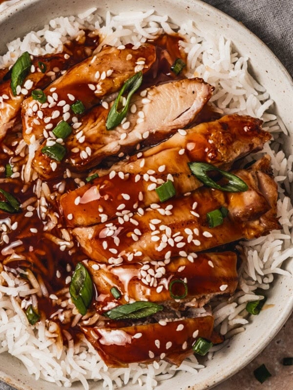 several slices of juicy chicken thigh topped with teriyaki sauce over a bed of white rice and sprinkled with sesame seeds and sliced green onions