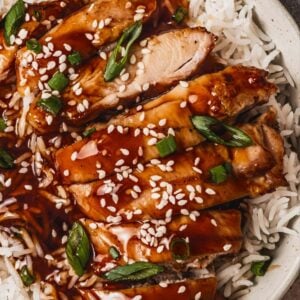 slices of juicy chicken thighs on top of white rice and topped with teriyaki sauce, sesame seeds and sliced green onions