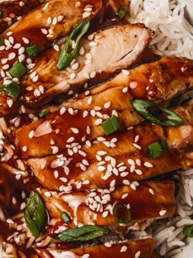 slices of juicy chicken thighs on top of white rice and topped with teriyaki sauce, sesame seeds and sliced green onions