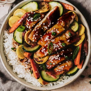 a bowl of rice topped with strips of teriyaki chicken and sauteed vegetables