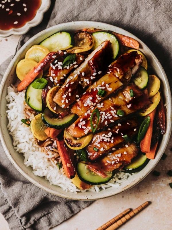 a bowl of rice topped with strips of teriyaki chicken and sauteed vegetables