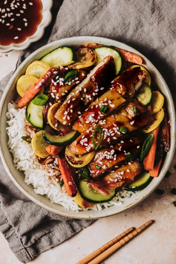 a bowl of rice topped with strips of teriyaki chicken and sauteed vegetables