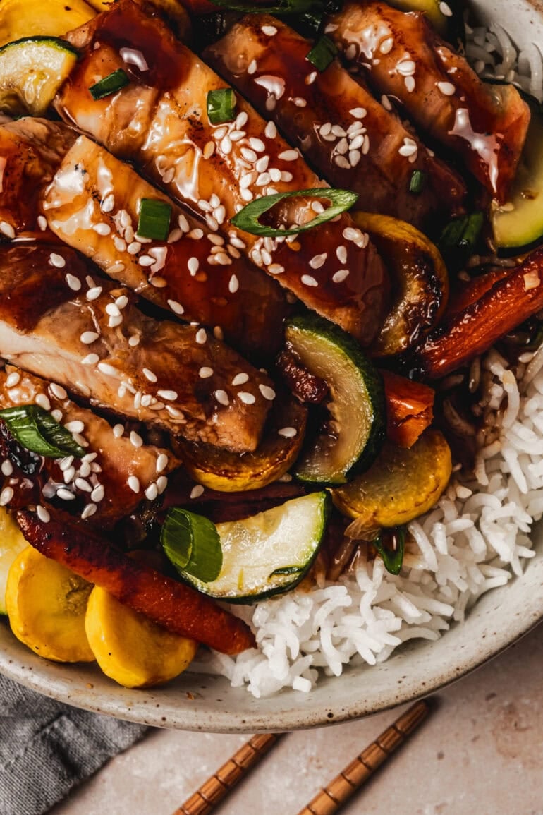 a bowl of white rice topped with sauteed vegetables and strips of teriyaki chicken