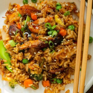 a photo of a dinner plate full of a teriyaki chicken casserole including fried rice, large chunks of chicken and assorted vegetables with chopsticks sitting on the side.