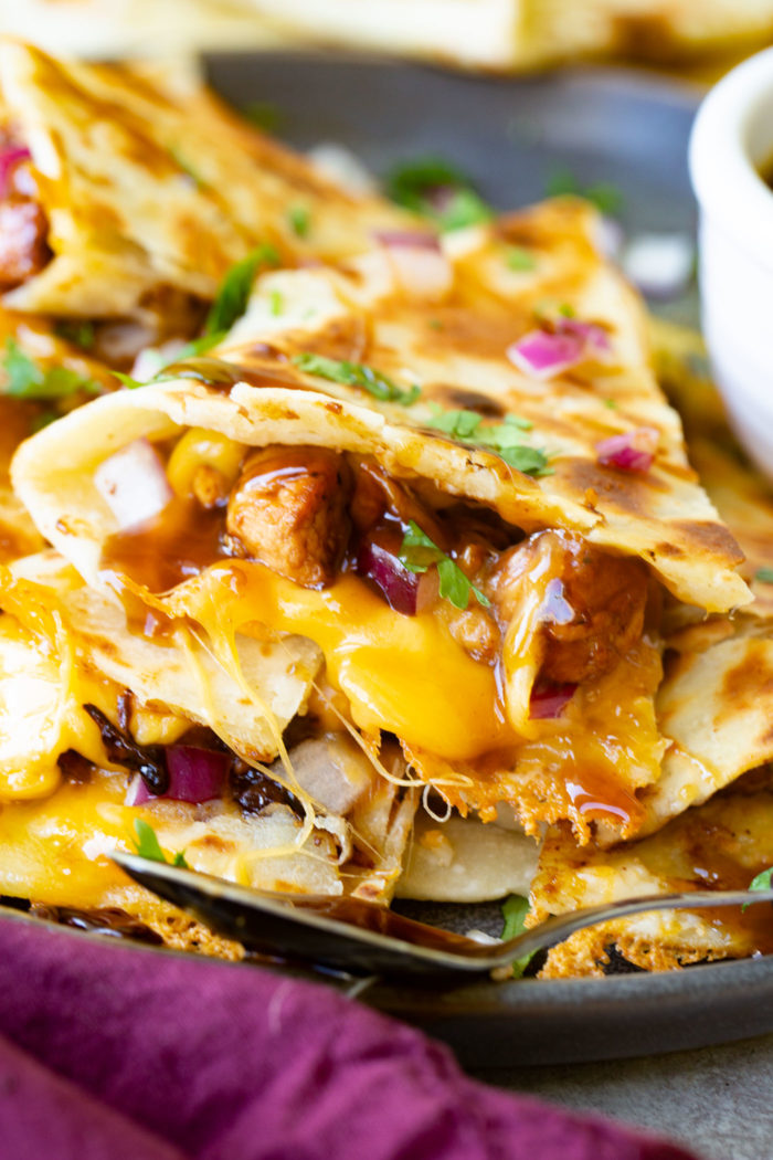 A photo of a slice of teriyaki chicken quesadilla garnished with minced red onion and chopped fresh cilantro.