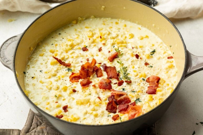 A pan of creamy, golden creamed corn topped with crispy bacon and fresh herbs.