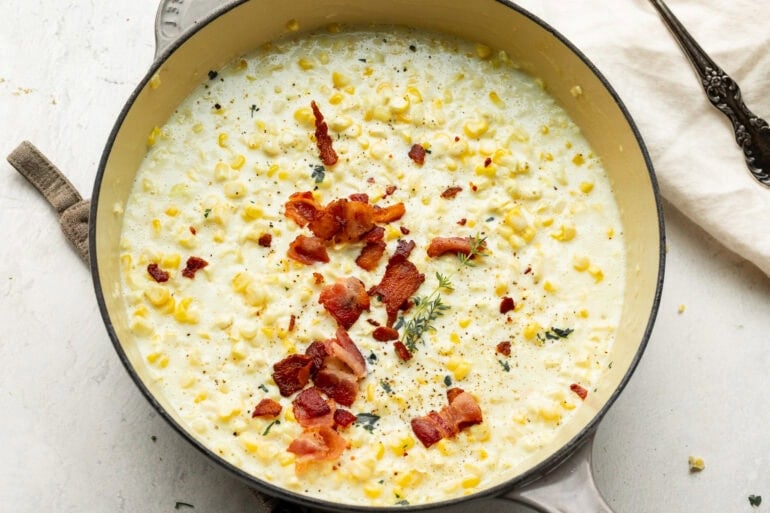 Overhead view of warm, creamy corn topped with bacon and fresh herb sprinkles.