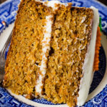 A photo of a slice of two layer carrot cake laying on its side on a blue and white plate.