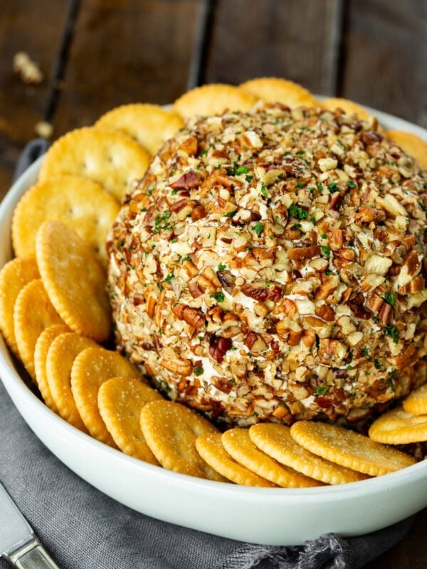 a photo of a large cheese ball coated in chopped pecans and minced fresh parsley surrounded by a bunch of Ritz crackers.