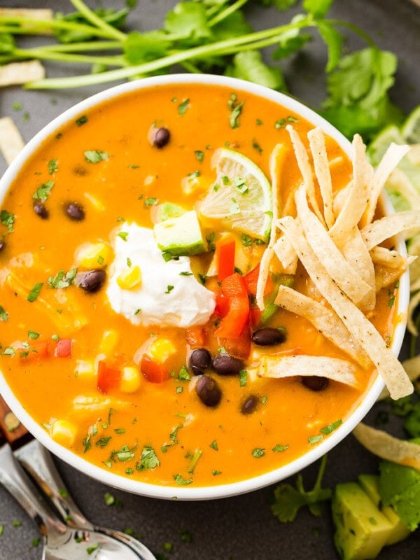 An aerial photo of a white bowl of chicken tortilla soup topped with sour cream, a lime wedge, and tortilla strips.