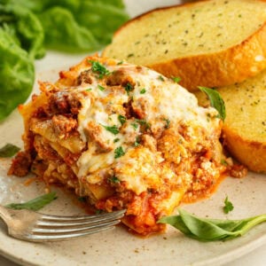 Slice of homemade crockpot lasagna served with garlic bread and salad