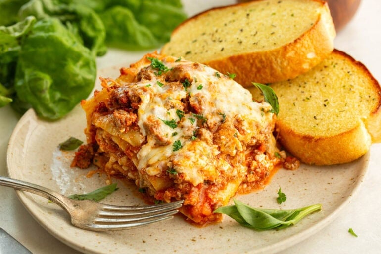 Slice of homemade crockpot lasagna served with garlic bread and salad
