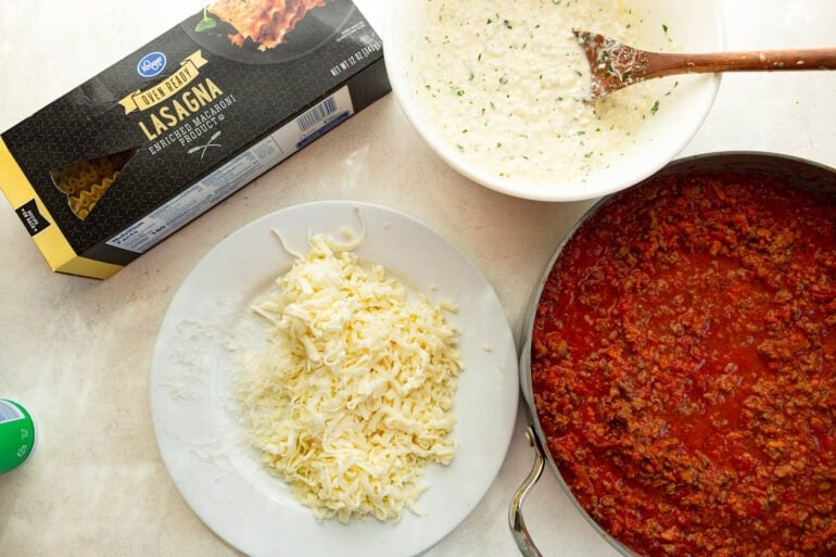 all the ingredients for easy crockpot lasagna including marinara sauce, lasagna noodles, cottage cheese mozzarella and ground beef with italian sausage