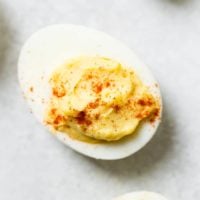 A grey board with a single deviled egg with paprika sprinkled on the top which makes the best deviled eggs ever!
