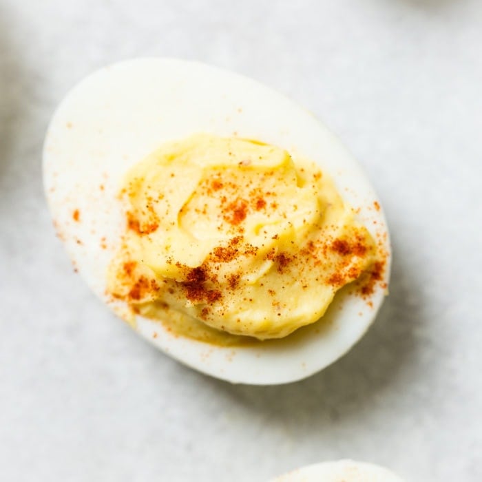 A grey board with a single deviled egg with paprika sprinkled on the top which makes the best deviled eggs ever!