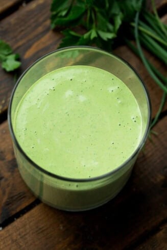 a photo taken over the top of a clear glass container full of creamy basil salad dressing
