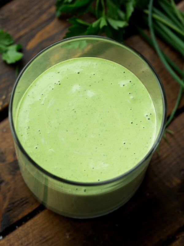 a photo taken over the top of a clear glass container full of creamy basil salad dressing