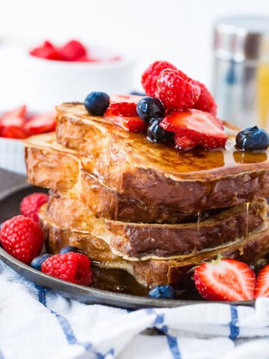 A photo of how to make french toast with a stack of french toast covered in dripping syrup and fresh berries.