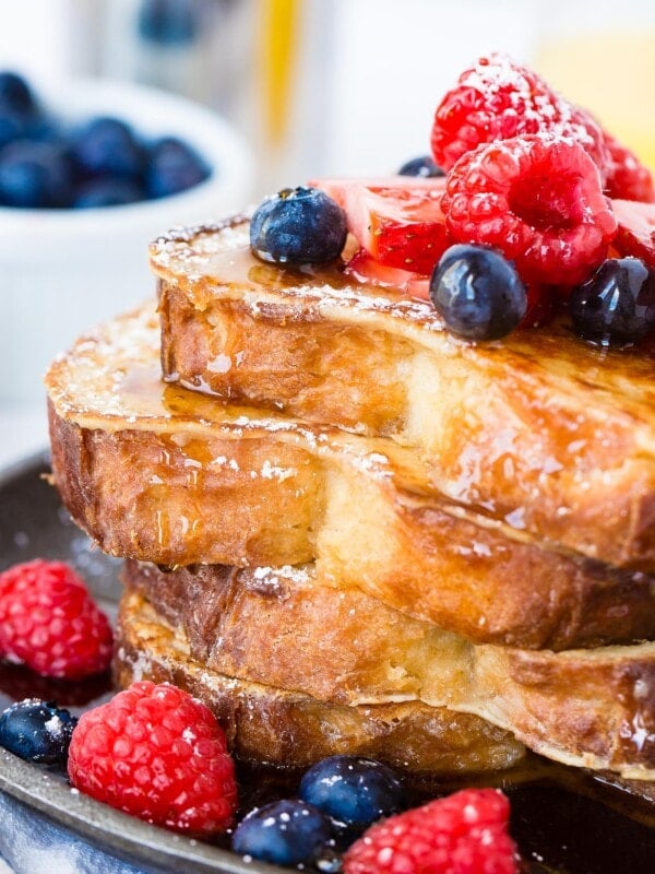 A photo of a stack of 4 perfectly made french toast slices dripping with syrup and fresh berries. How to Make French Toast