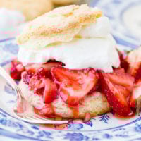A closeup photo of homemade strawberry shortcake recipe on a blue and white plate with a sweet biscuit, juicy strawberries, and whipped cream.