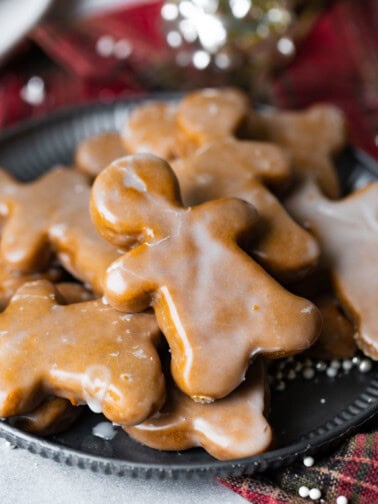 a photo of a lightly glazed gingerbread man cookie on top of a pile of other gingerbread men cookies.