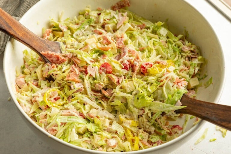 a large bowl of grinder salad being tossed with wooden spoons