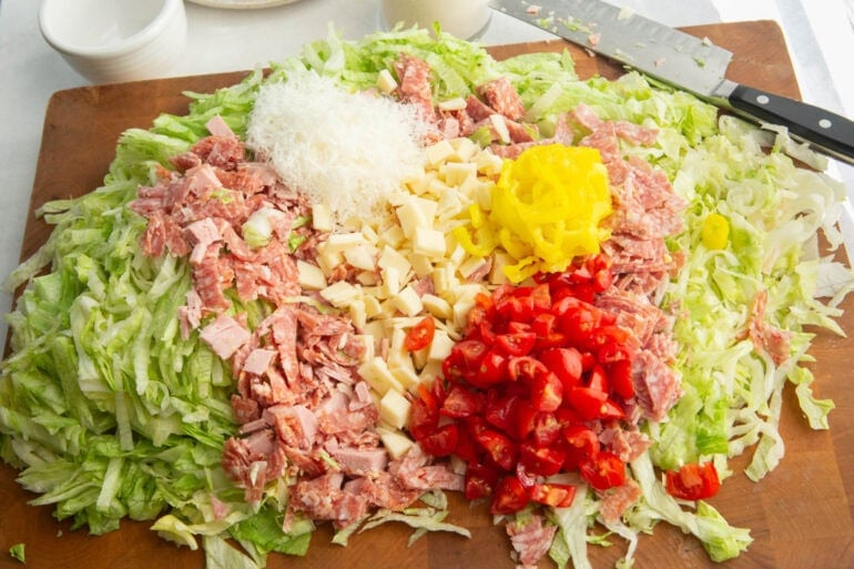 all the ingredients for grinder salad sitting a wooden cutting board ready to be tossed