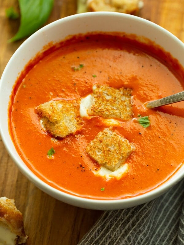 a photo of a bowl of tomato basil soup with three grilled cheese bites sitting on top and a spoon in the bowl