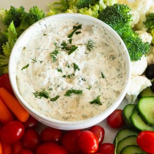 a small bowl of creamy garlic herb veggie dip surrounded by fresh vegetables for dipping