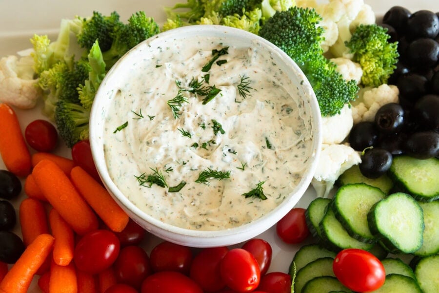 a small bowl of creamy garlic herb veggie dip surrounded by fresh vegetables for dipping