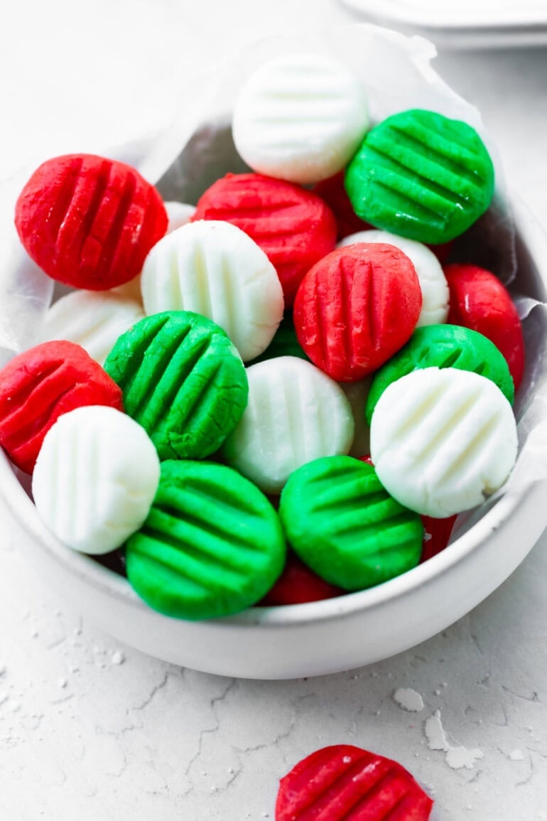 A small white bowl filled with butter mints pressed with a fork into green, red and white colors
