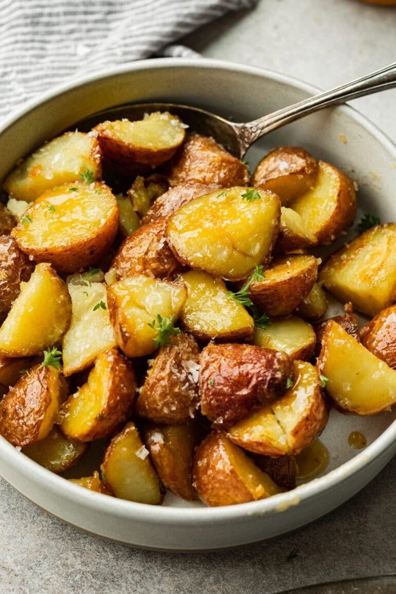 Crispy caramelized red potatoes are placed in a minimalist white bowl with their golden edges contrasting sharply with the smooth surface below.