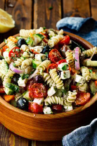 a photo of a large wooden bowl of greek pasta salad