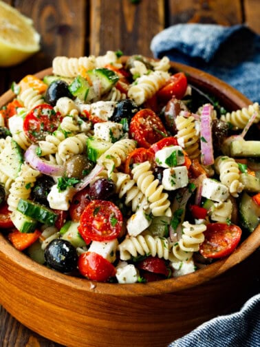 a photo of a large wooden bowl of greek pasta salad