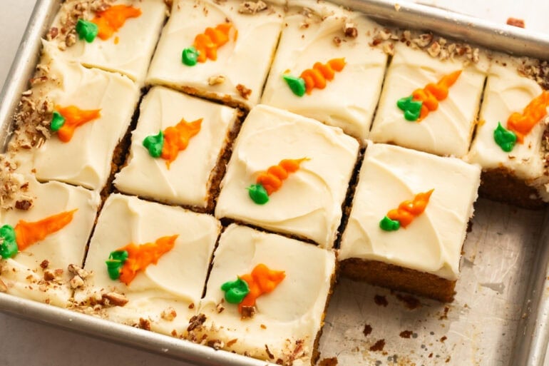 a whole carrot cake topped with cream cheese frosting cut into individual slices with each piece topped with a little piped carrot