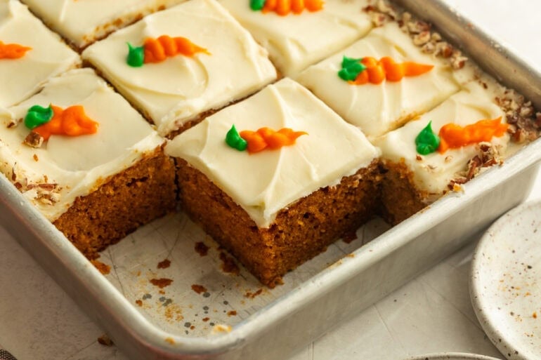 a baking pan with carrot cake slices in it topped with cream cheese frosting with a little carrot piped on each piece