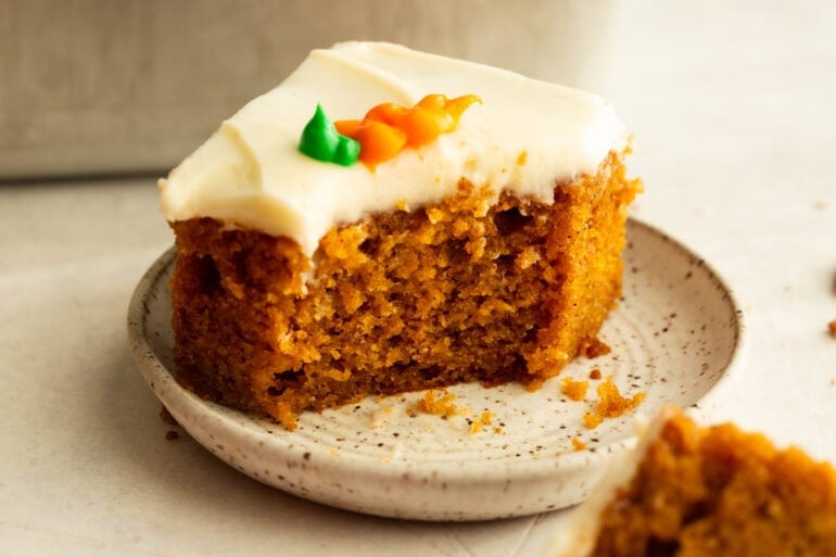 a piece of moist carrot cake with a bite taken out of one corner, topped with cream cheese frosting