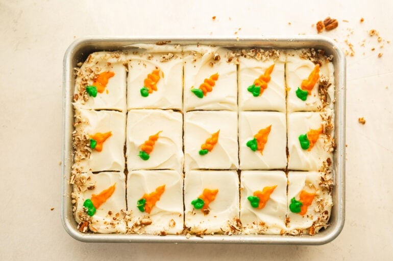 a baked and frosted carrot cake sliced into pieces with a little carrot piped on each piece