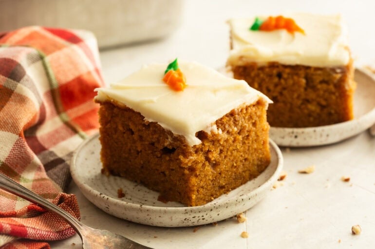 a slice of moist carrot cake on a small dessert plate topped with cream cheese frosting on top
