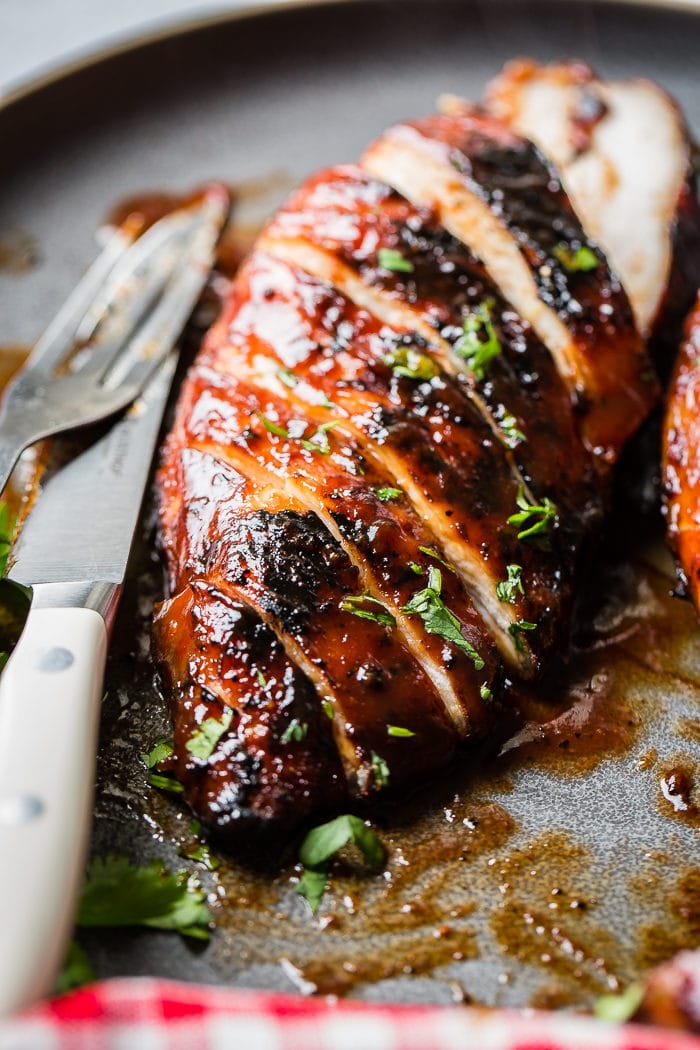 A grey plate with a sliced BBQ chicken sprinkled with parsley