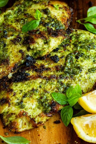a photo taken over the top of two grilled chicken breasts coated in basil sitting on a cutting board with lemon wedges sitting next to them