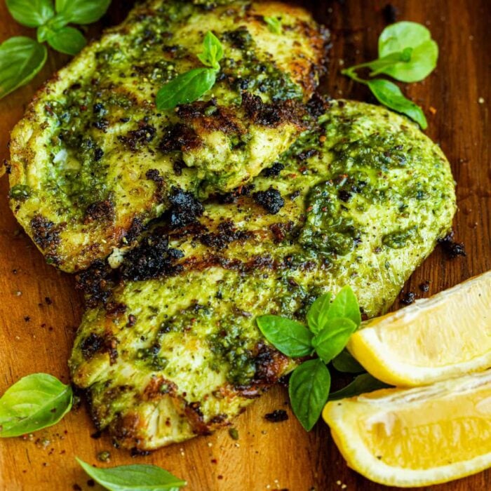 a photo taken over the top of two grilled chicken breasts coated in basil sitting on a cutting board with lemon wedges sitting next to them
