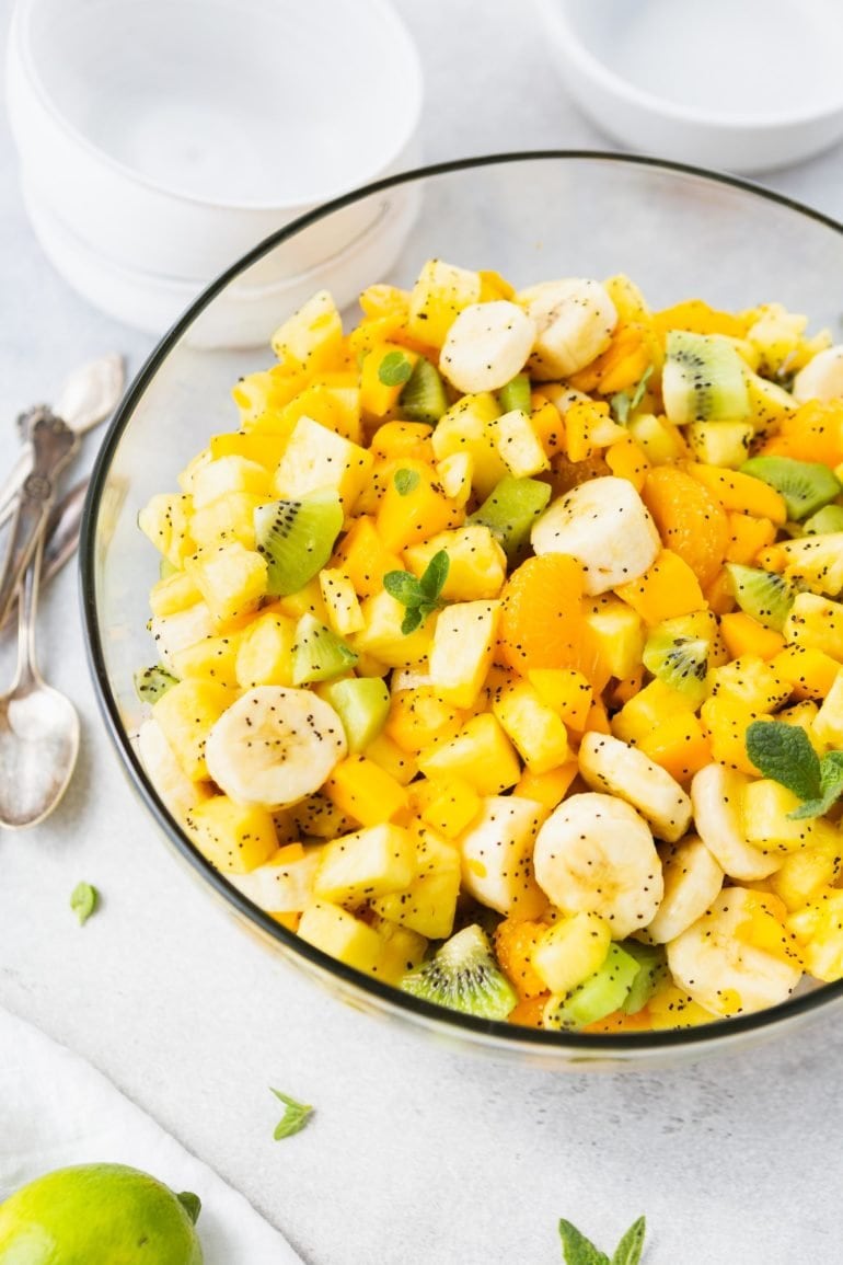 a photo taken from above of a glass bowl full of chopped up tropical fruits covered in a honey lime poppy seed dressing.