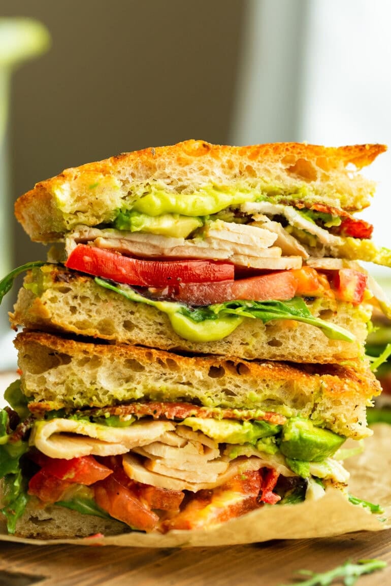 a sandwich cut in half so you can see the inside piled with tomatoes, turkey, avocado and bacon