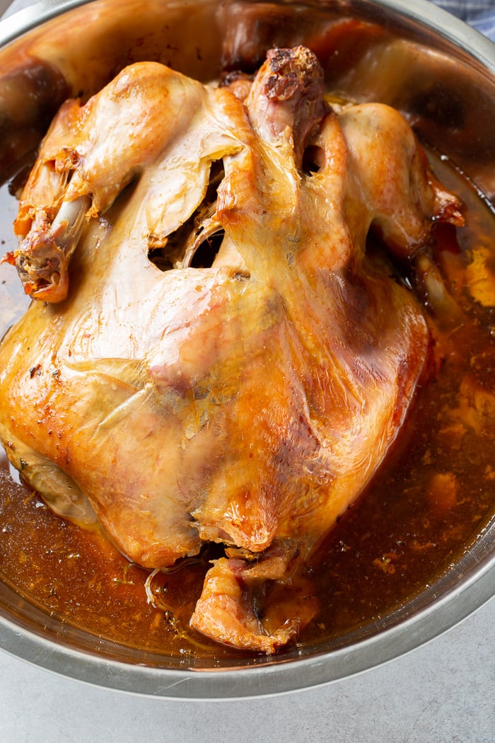 a photo of a whole turkey that is golden brown and sitting in its juices in a large metal mixing bowl