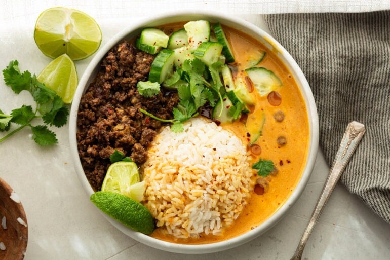 Overhead view of a beef broth bowl with caramelized ground beef, rice, coconut curry broth and fresh cucumber