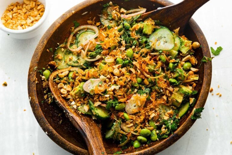 a large wooden bowl of crispy rice salad with wooden spoons tossing the salad