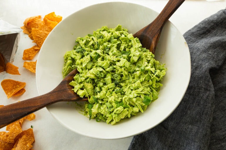 chopped green goddess salad being tossed in a large white serving bowl with wooden spoons